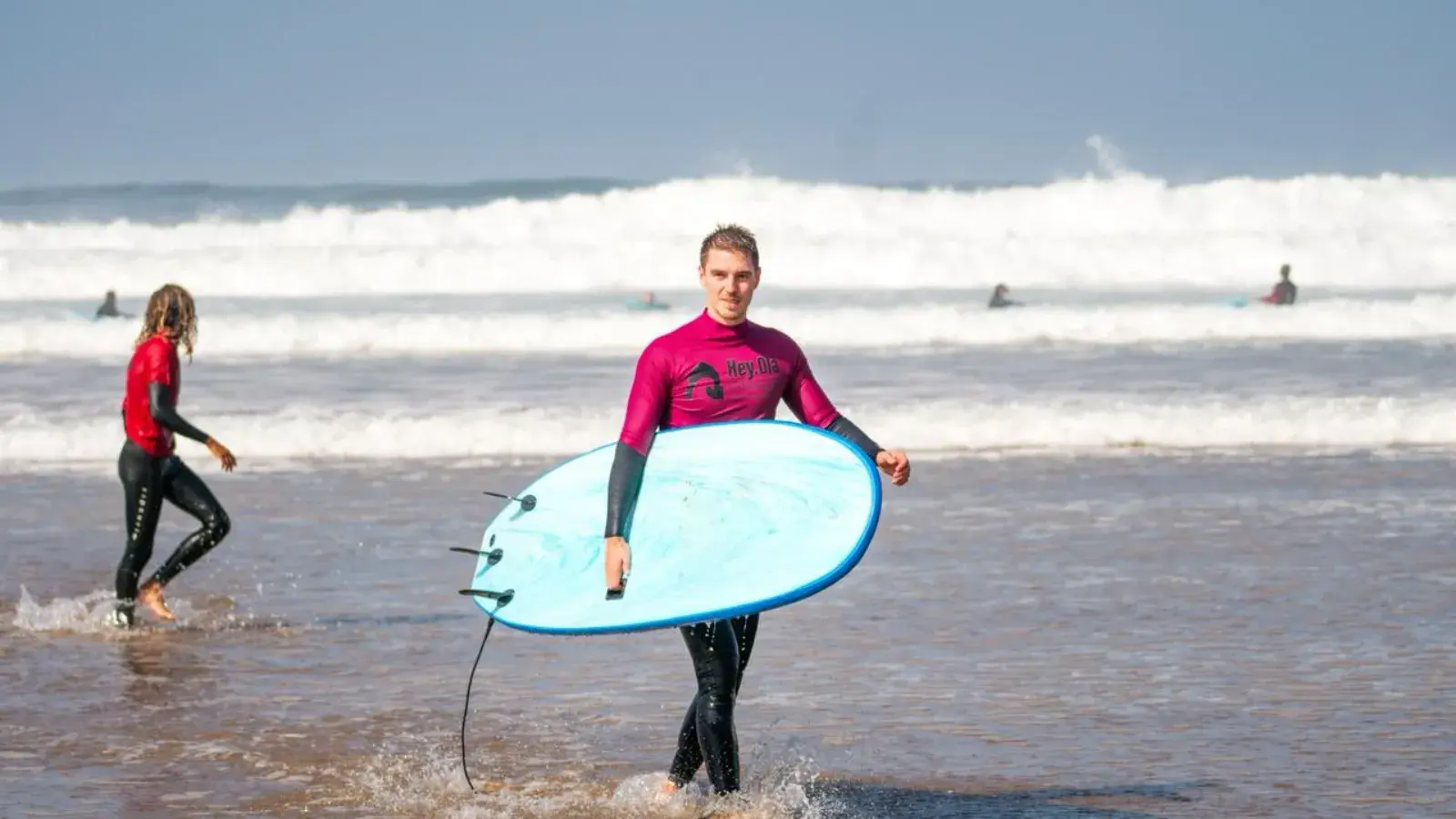 Deux surfeurs débutants sortent de l’eau à Mirleft, planche en mousse sous le bras