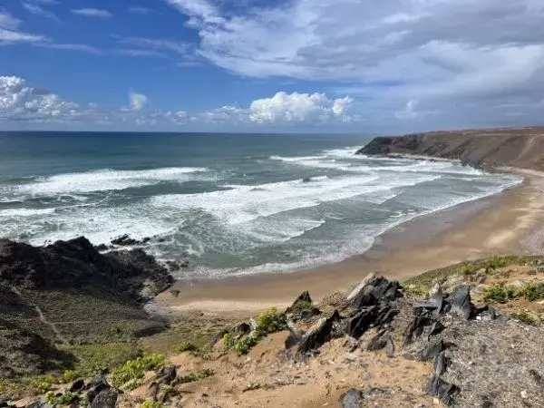 Vue sur les falaises ocre de Mirleft plongeant vers une plage de sable déserte avec des vagues régulières sous un ciel de fin d'après-midi